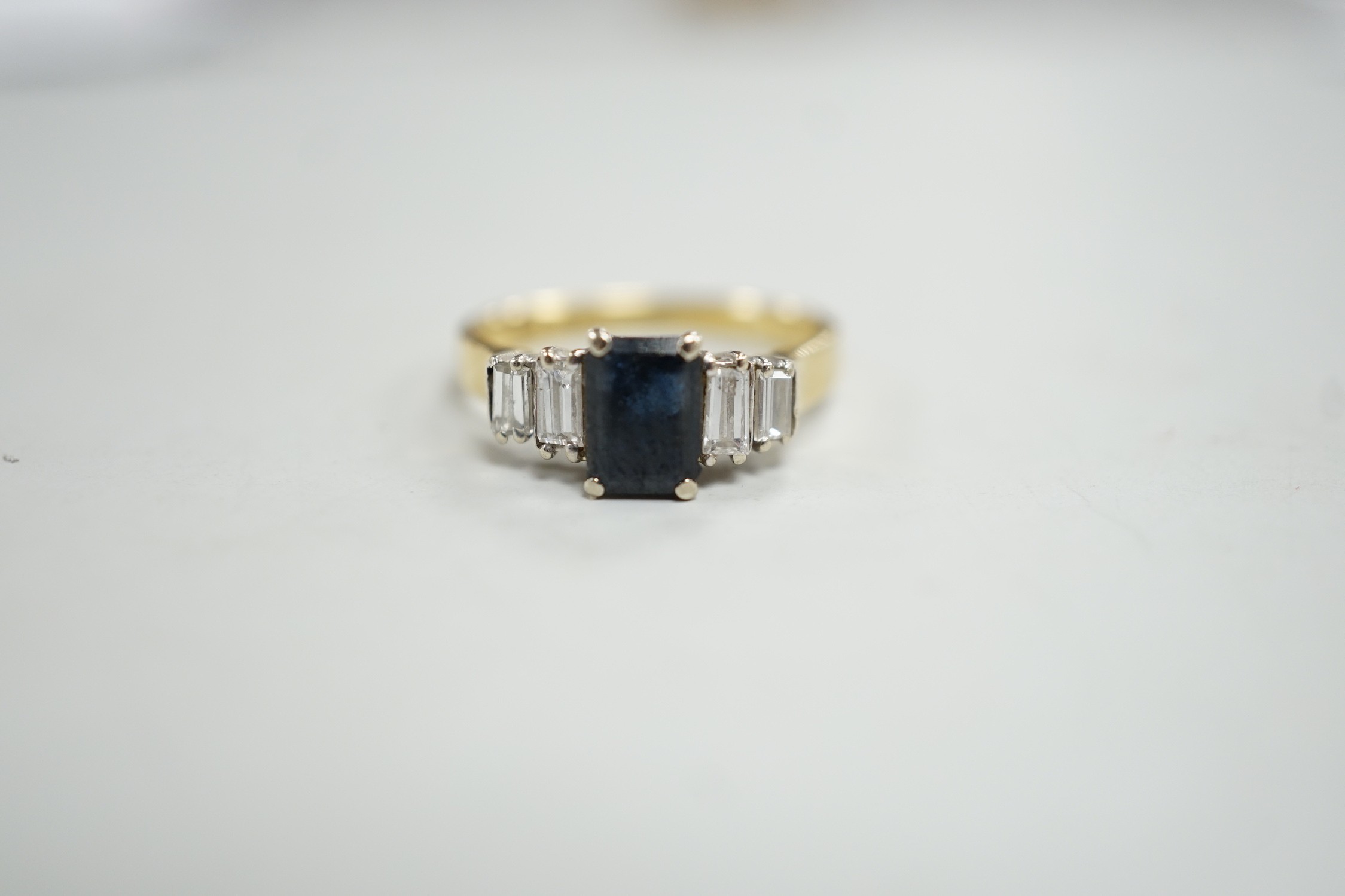 A modern 18ct gold and single stone emerald cut sapphire set ring, with graduated baguette cut diamond set shoulders, size J/K, gross weight 3.1 grams.